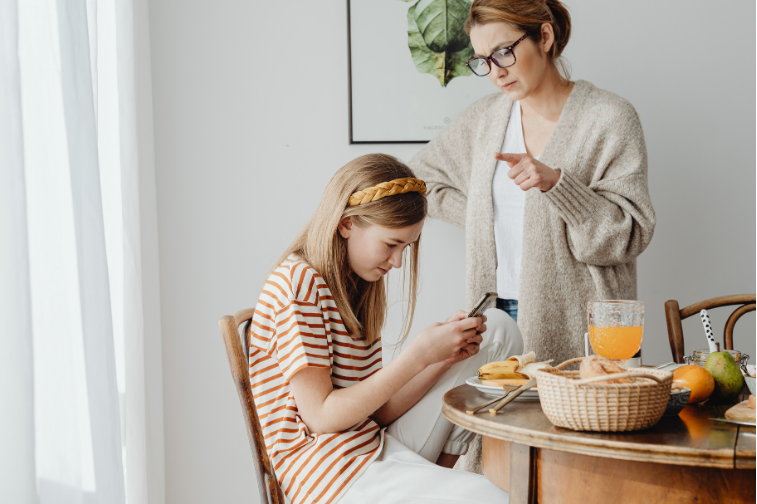 mom talking to teenage daughter on phone at table